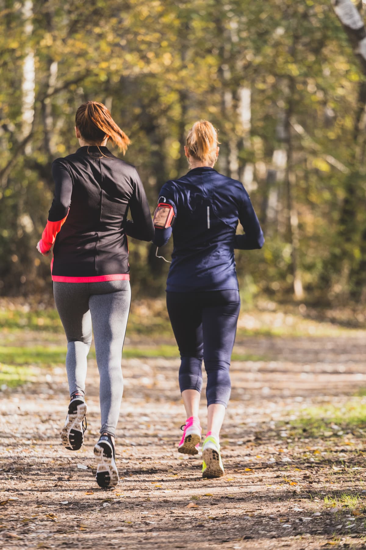 Two women running together through a sunlit park